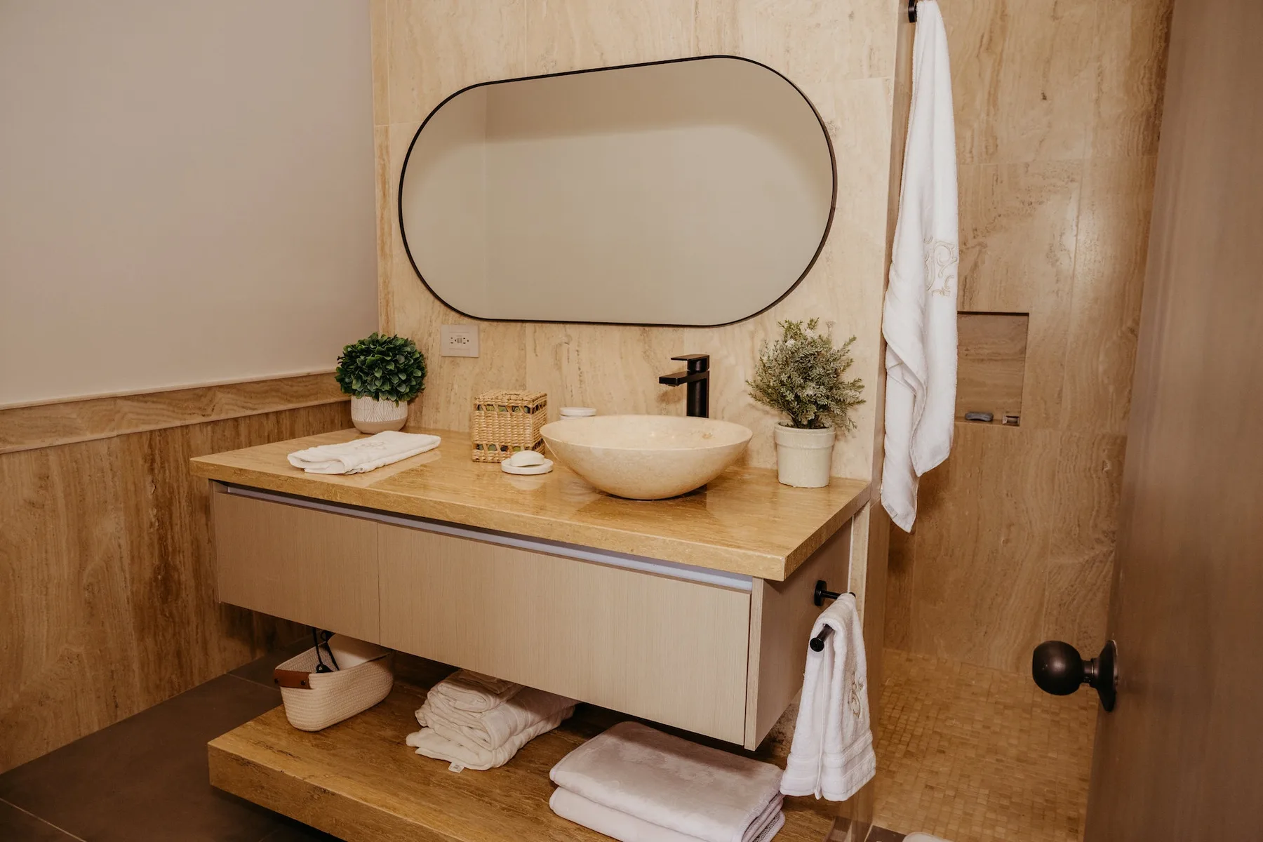 Un tocador de baño con lavabo sobre encimera, espejo ovalado y muebles de madera.