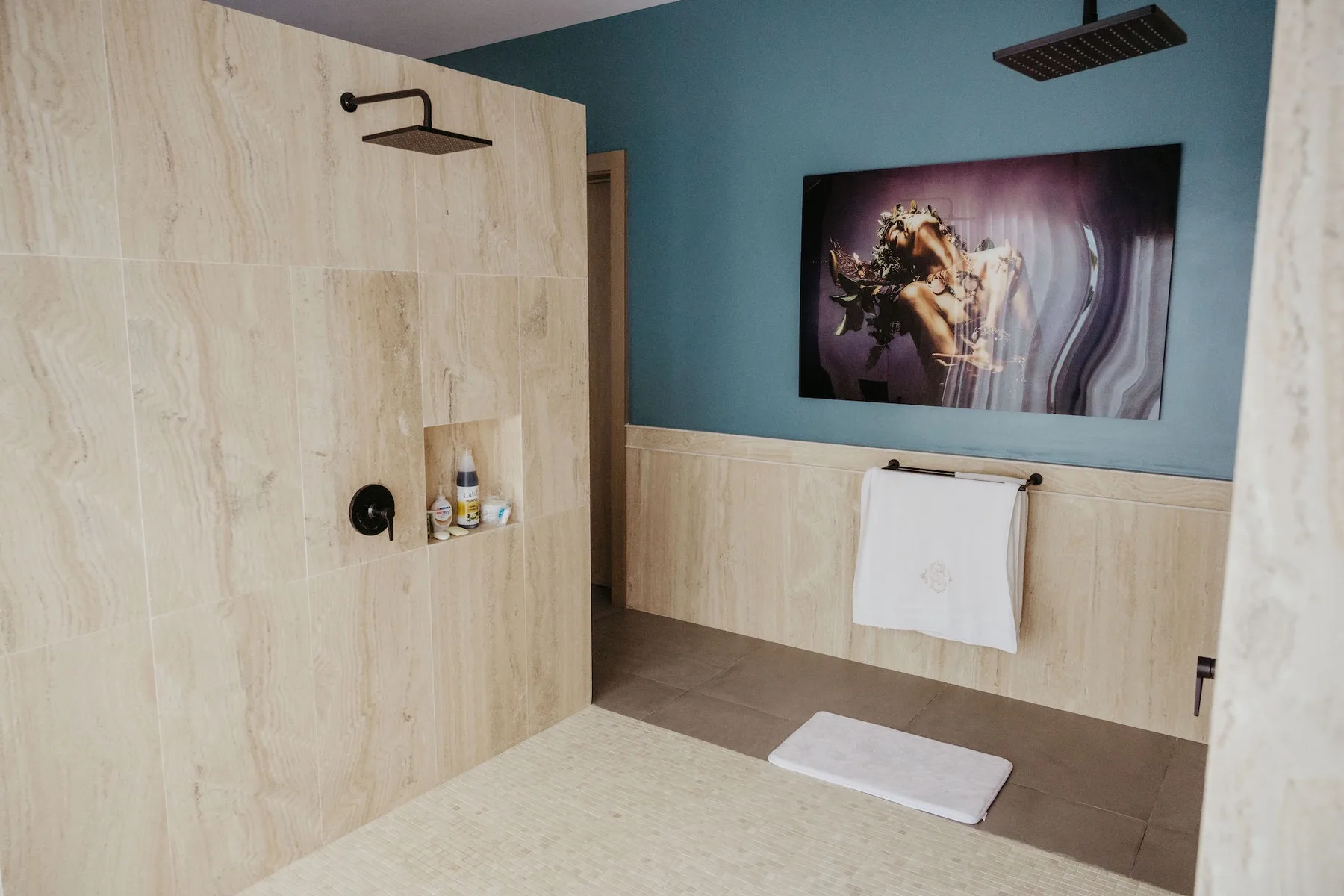 Baño revestido de azulejos, con una ducha de pared y una toalla bajo una obra enmarcada.