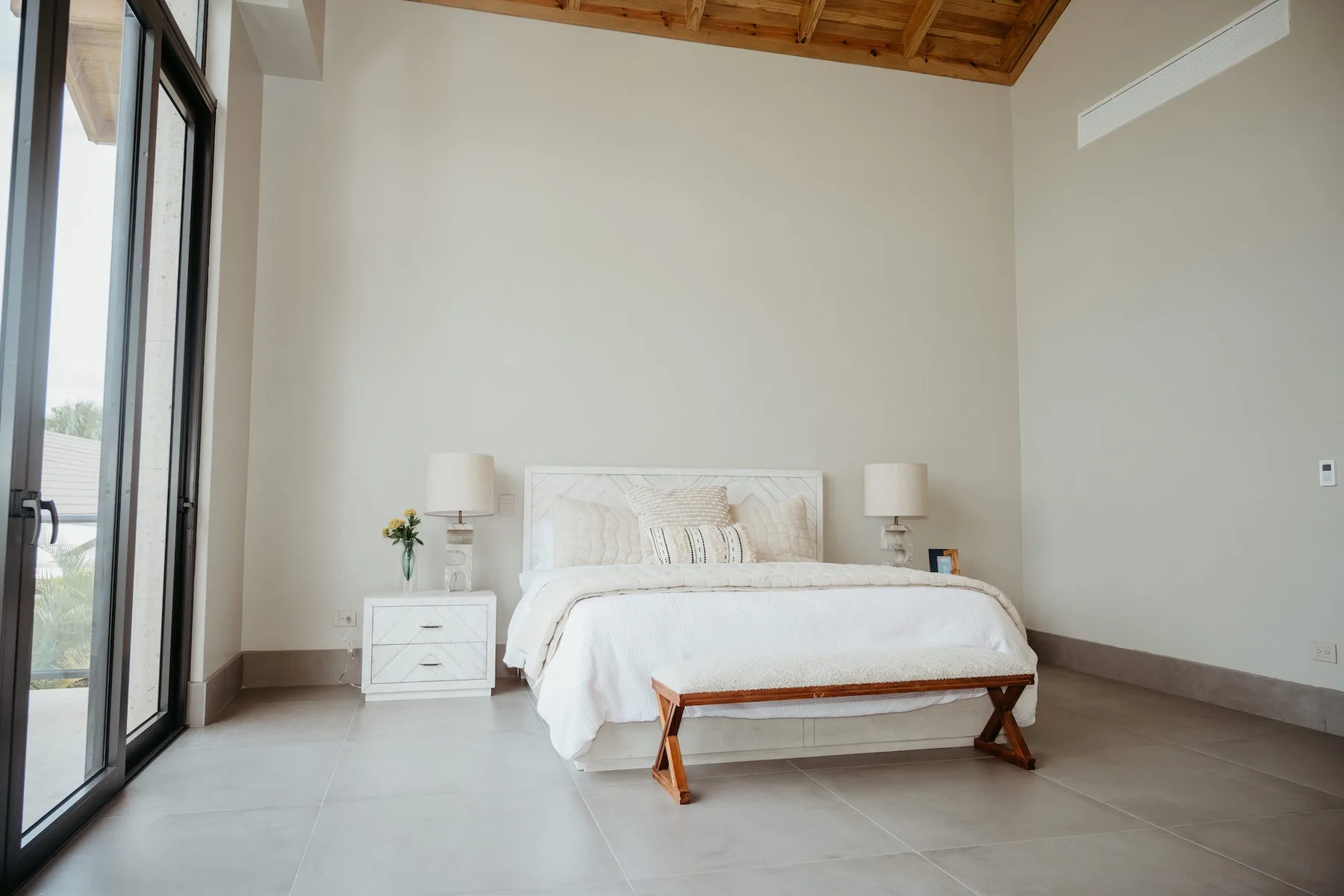 Un dormitorio luminoso con una cama y mesitas junto a ventanas altas.