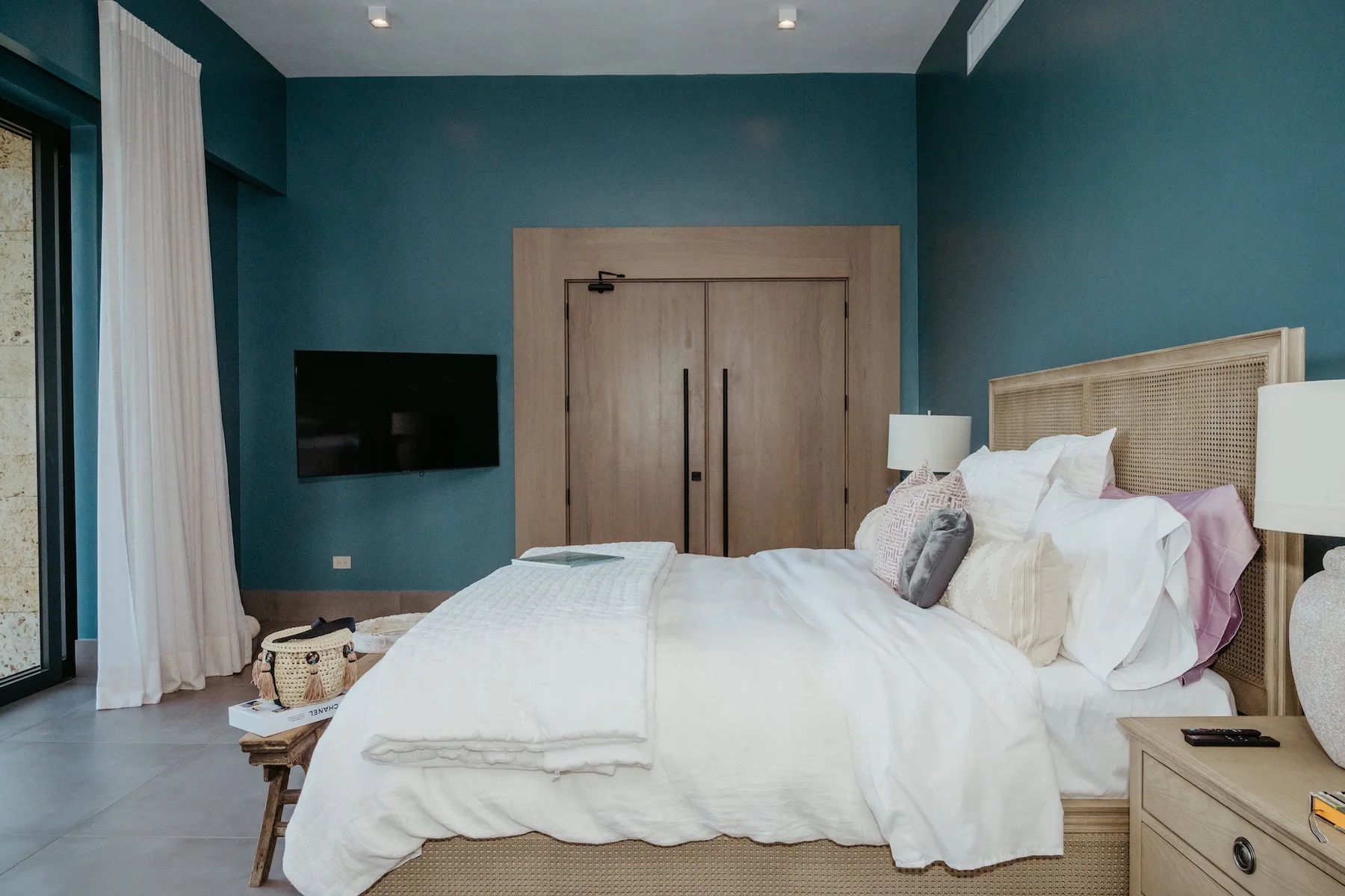 Un dormitorio con una cama blanca, paredes verde azulado y un televisor en la pared.