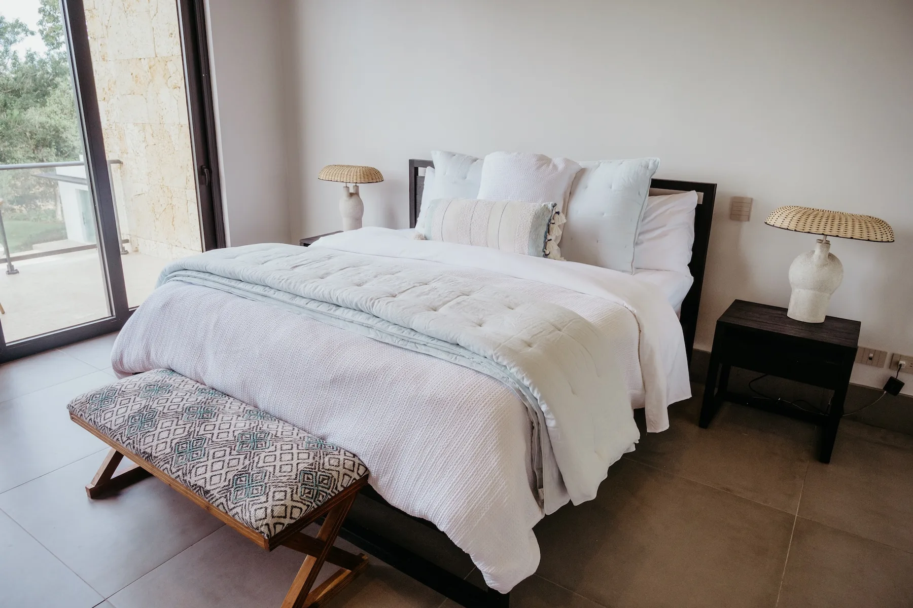 Dormitorio con una cama tendida y un banco a los pies.