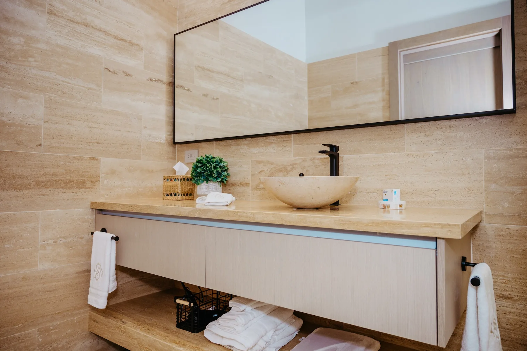 Un mueble de baño con lavabo y un espejo grande frente a paredes revestidas de azulejos.