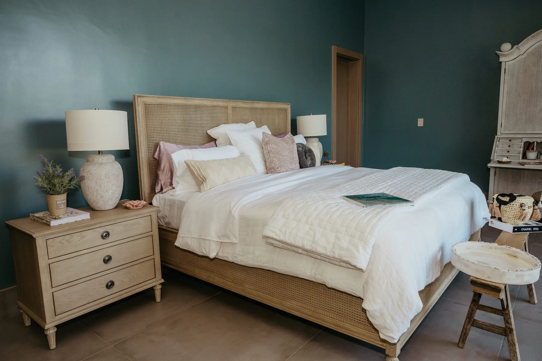 Un dormitorio con una cama tendida, una mesita de noche y paredes verde azulado.