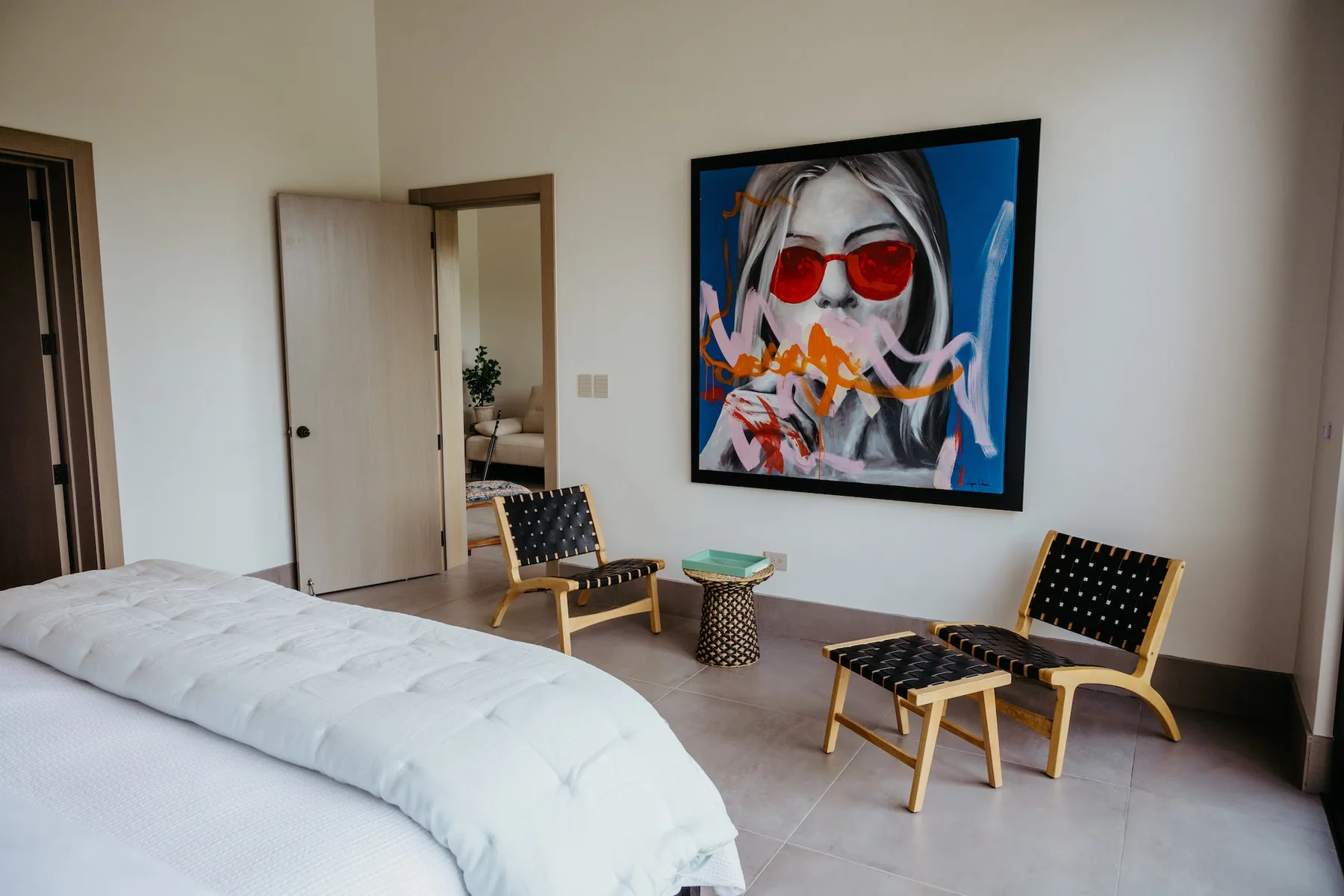 Un dormitorio con una cama, dos sillas y una obra colorida enmarcada.