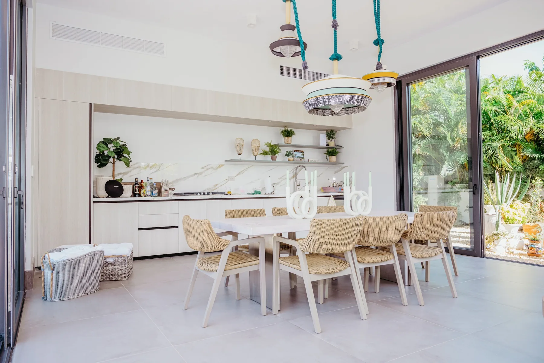 Un comedor luminoso con una mesa larga y asientos tejidos junto a grandes ventanales.