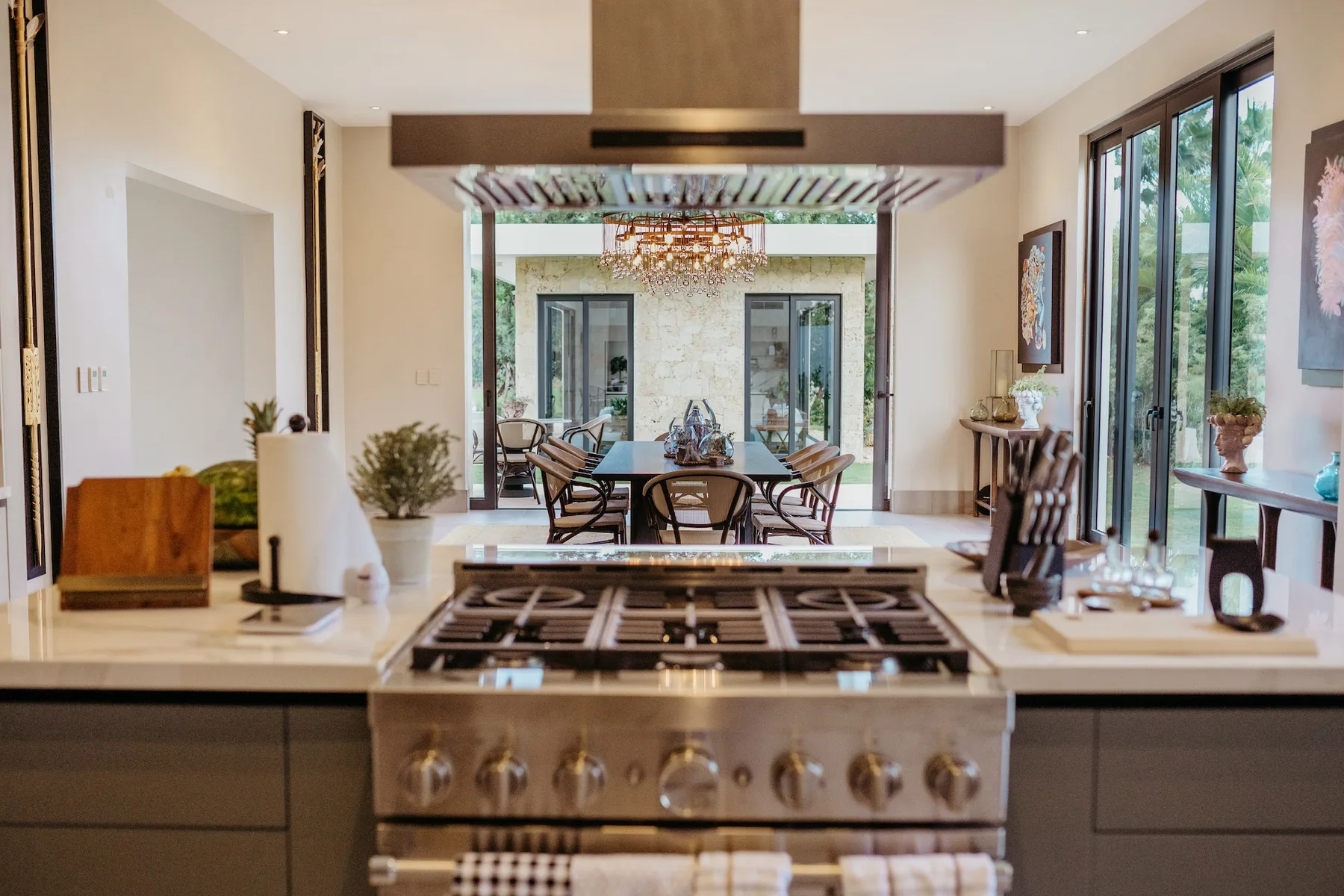 Una isla de cocina con una placa de cocción da a una mesa de comedor junto a grandes ventanas.