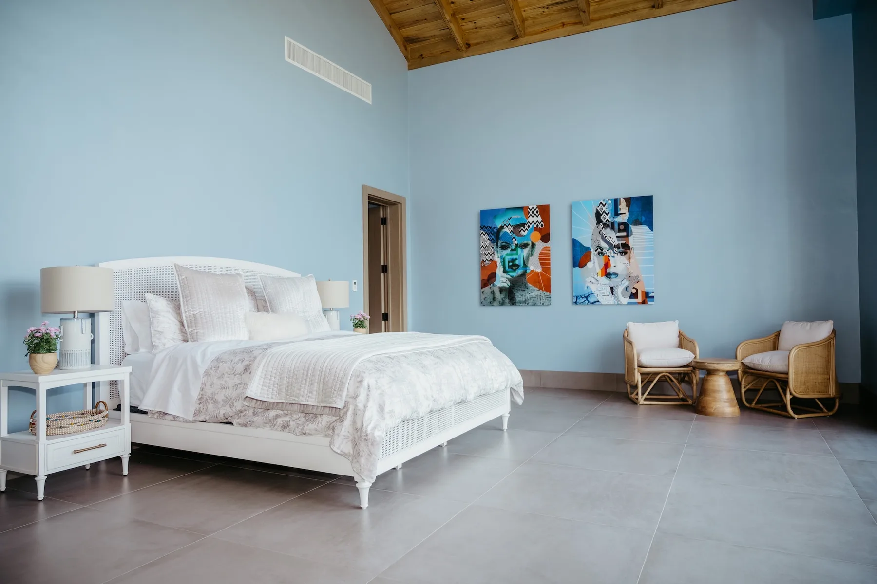 Un dormitorio con una cama grande y dos sillas bajo cuadros coloridos.
