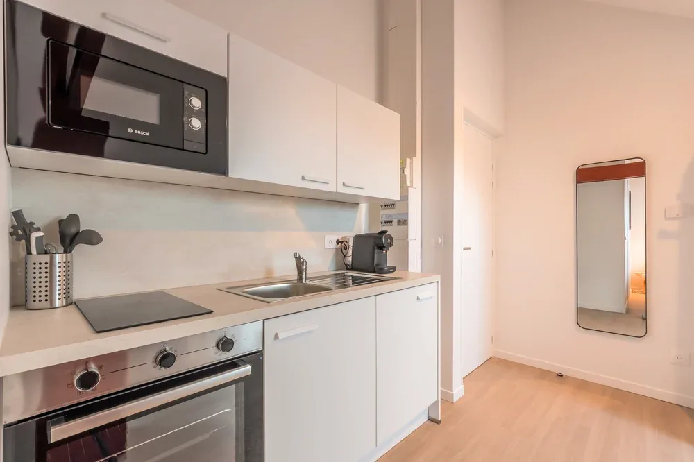 A compact kitchen with white cabinets, a cooktop, and a sink.
