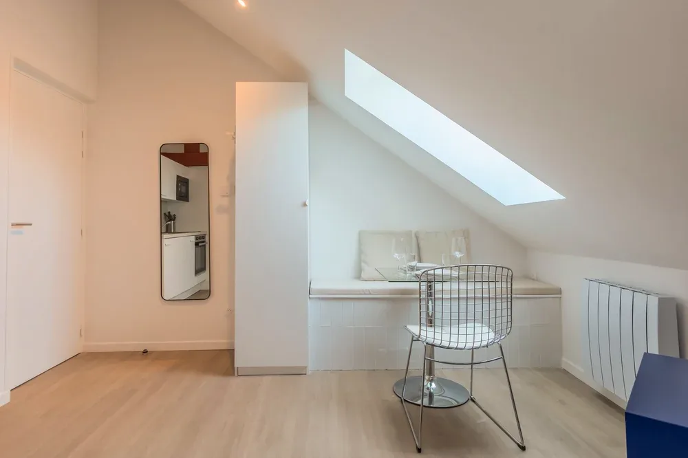 A bright attic room with a sloped ceiling, skylight, and small seating area.