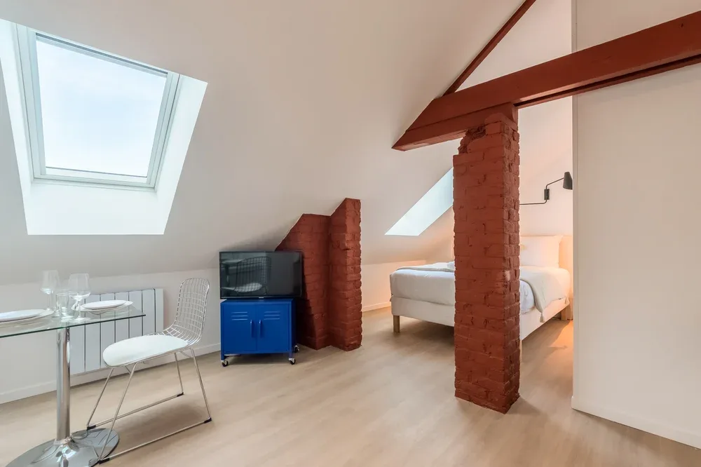A loft bedroom with a bed, skylights, and a small dining area.