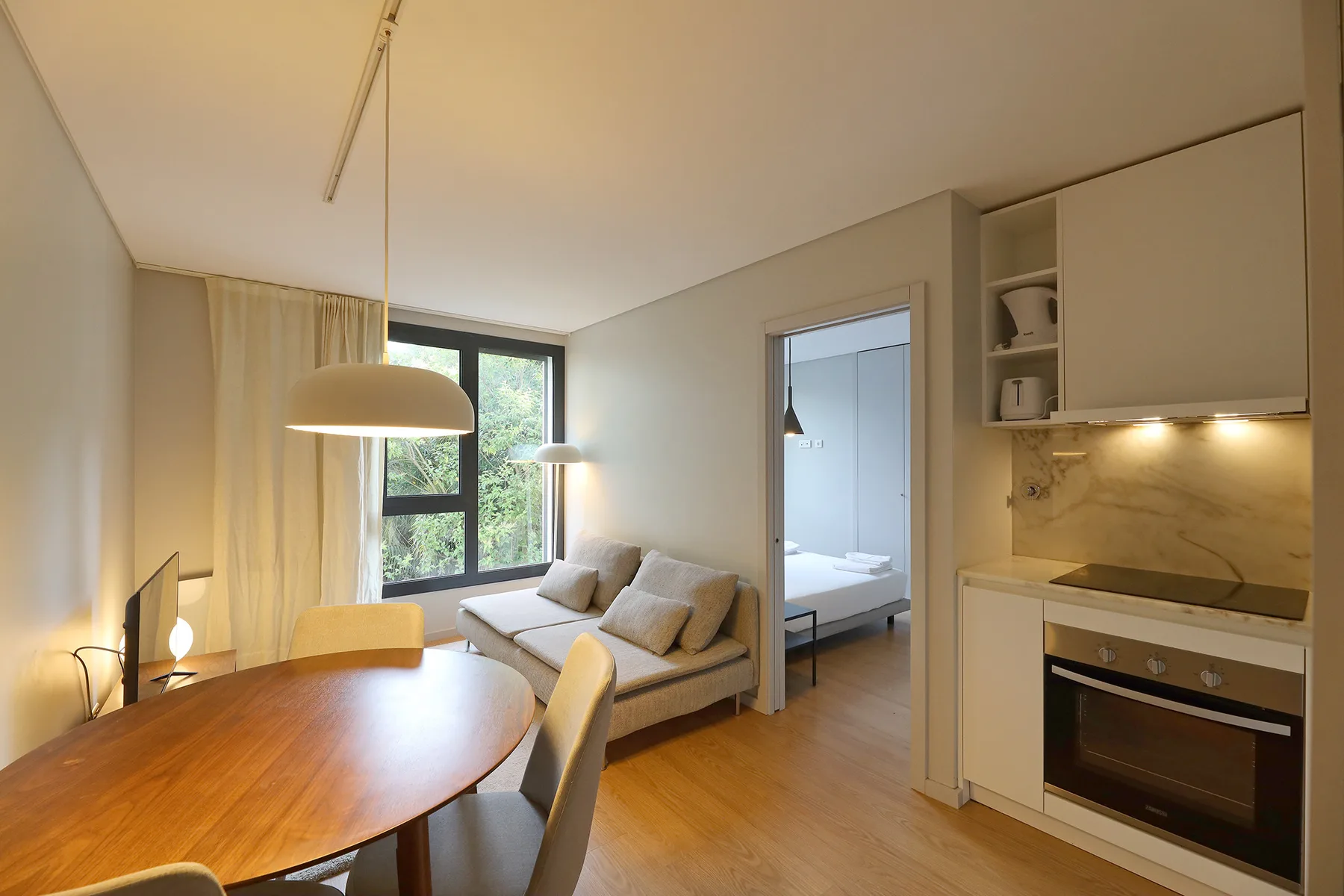 Una luminosa sala de estar y comedor con sofá, mesa y cocina pequeña.