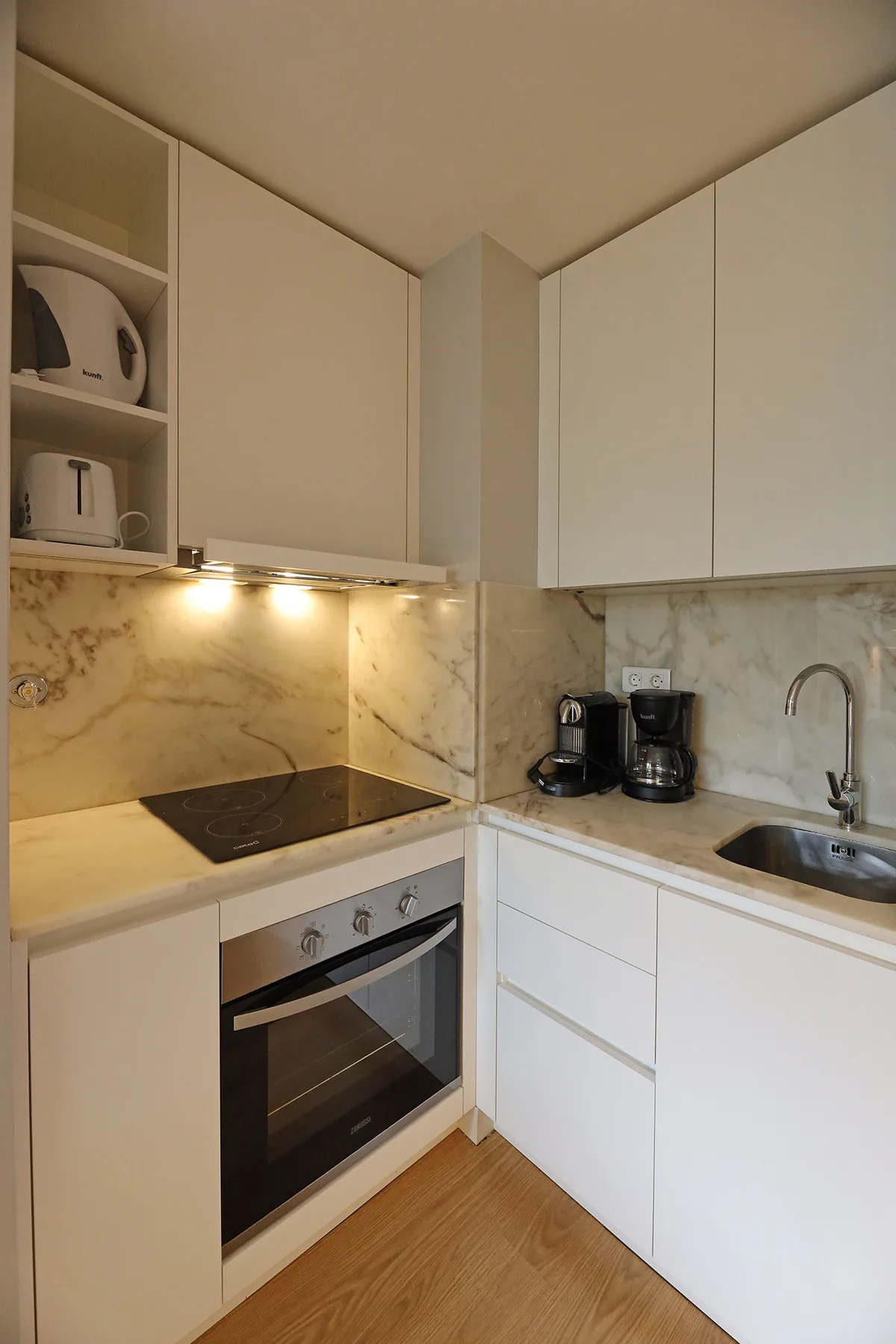 Una cocina compacta con armarios blancos, una placa de cocina y un fregadero.