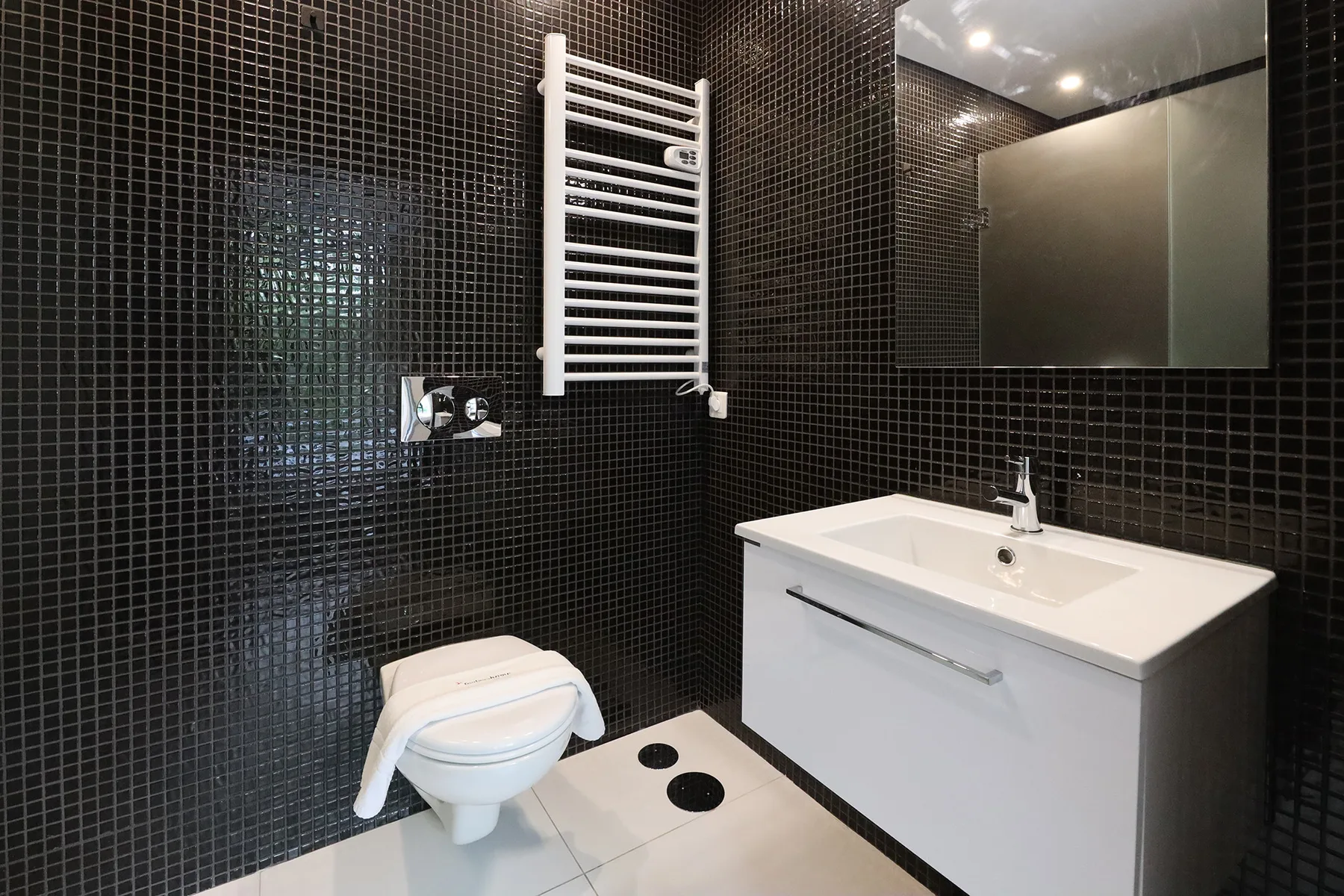 Un baño con lavabo, inodoro y paredes de azulejos oscuros.