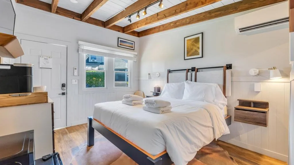 A bright bedroom with a neatly made bed and exposed wooden ceiling beams.