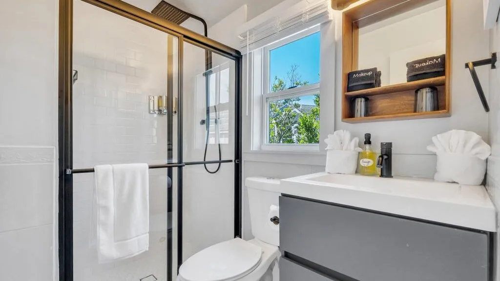 Un baño luminoso con ducha de vidrio, tocador y ventana.