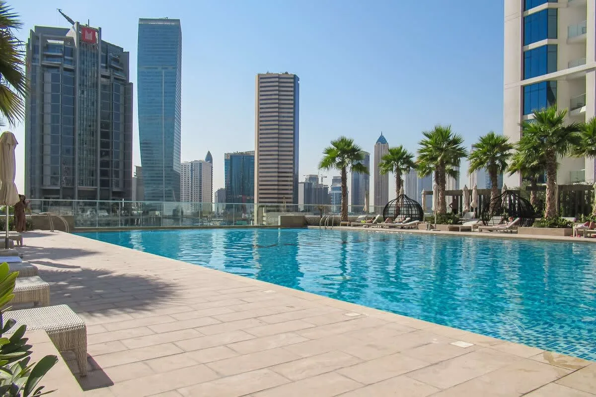 Una piscina en la azotea tiene vistas a modernos edificios y palmeras.