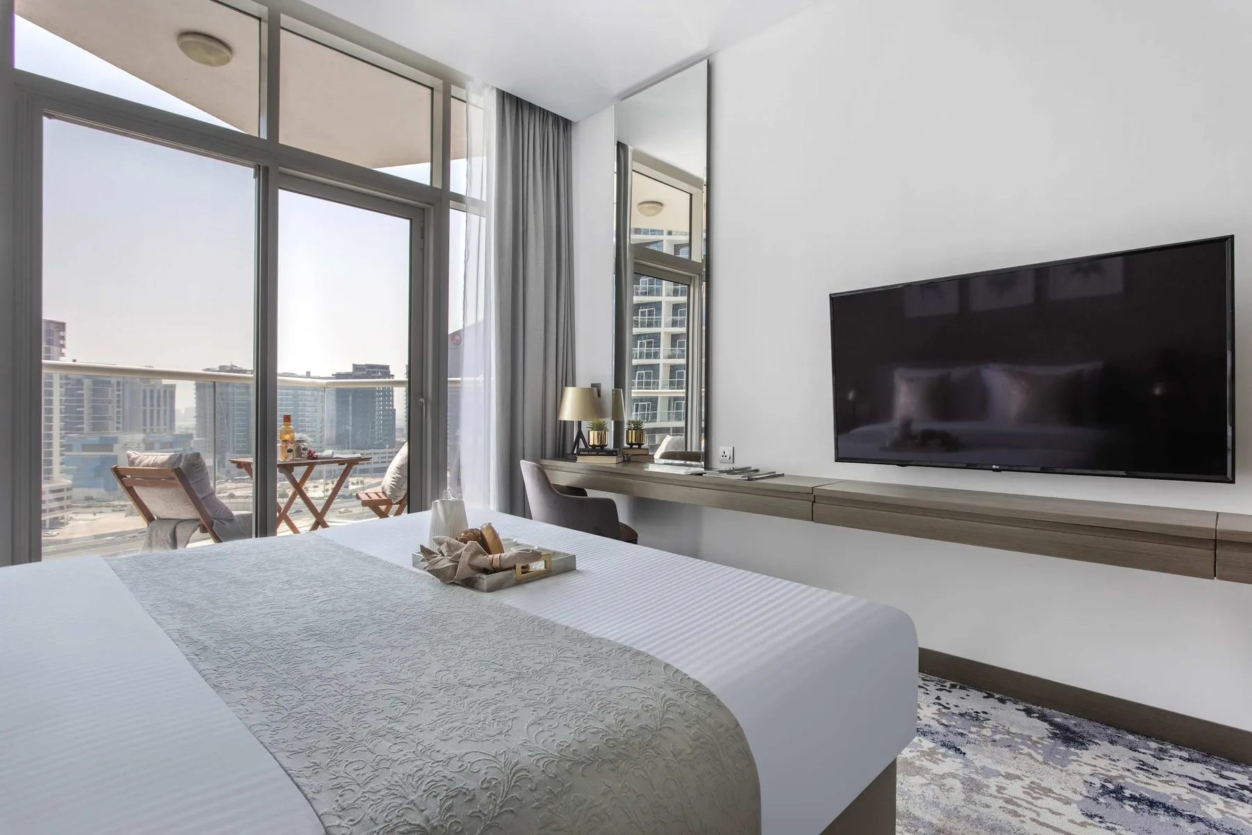 Dormitorio con una cama grande, ventanas de suelo a techo y un televisor en la pared.