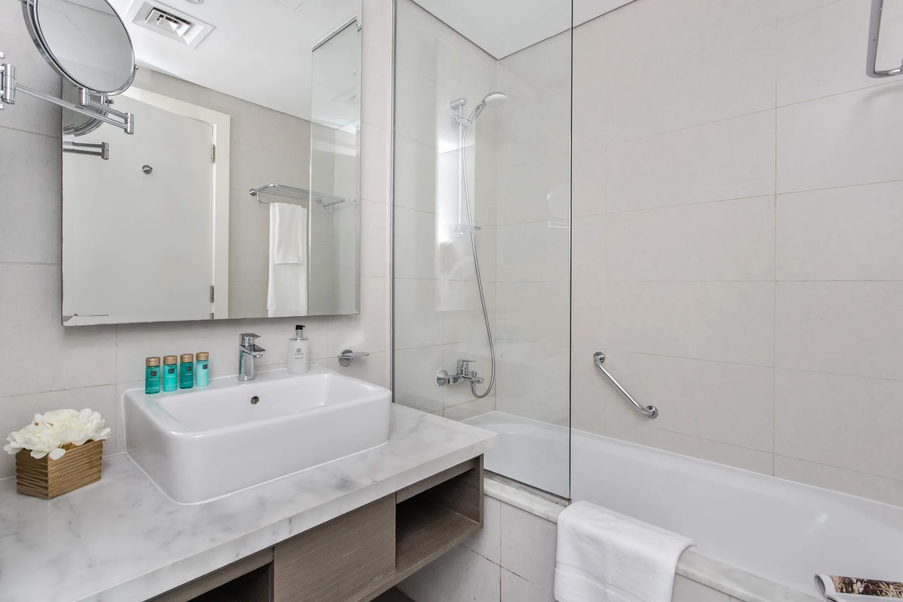 Un baño con lavabo, espejo y bañera con mampara de ducha de vidrio.