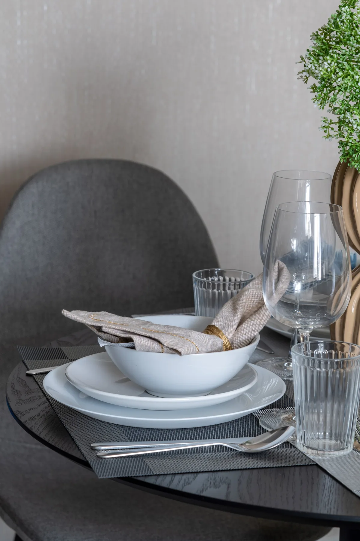 Una mesa de comedor está preparada con platos, servilletas dobladas, vasos y cubiertos.