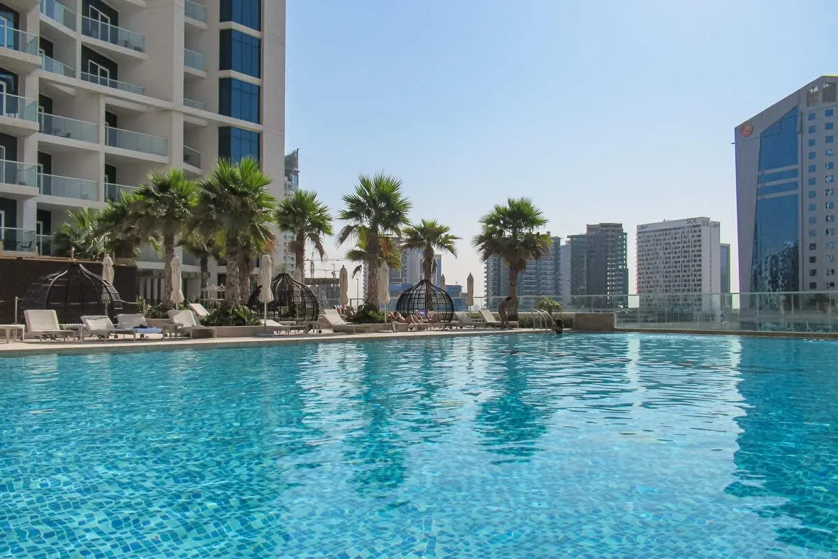 Una piscina en la azotea con palmeras y edificios de la ciudad al fondo.