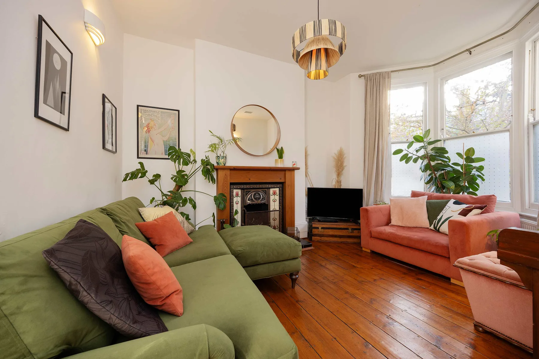 Una sala luminosa con asientos verdes, una chimenea y grandes ventanas.