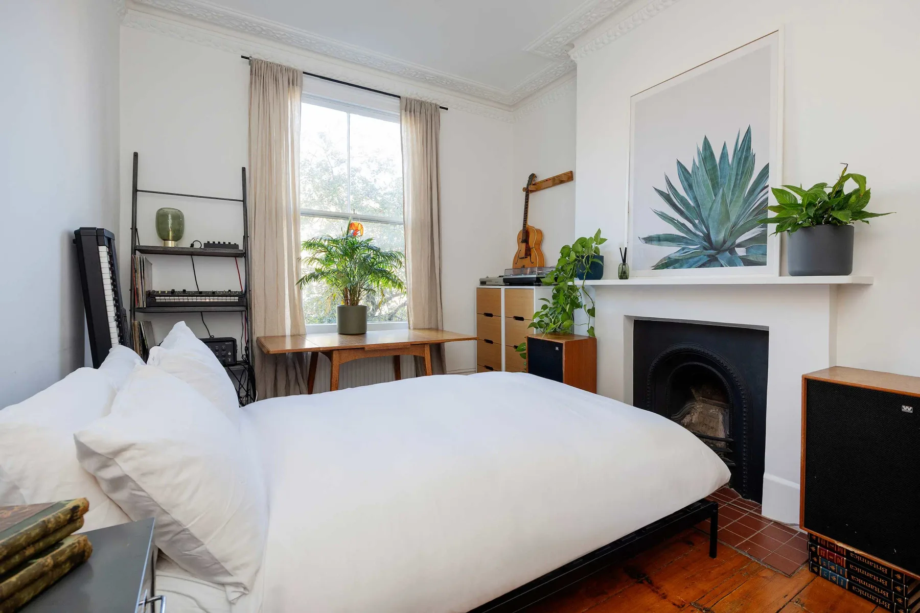 Un dormitorio con una cama, una chimenea y plantas junto a la ventana.