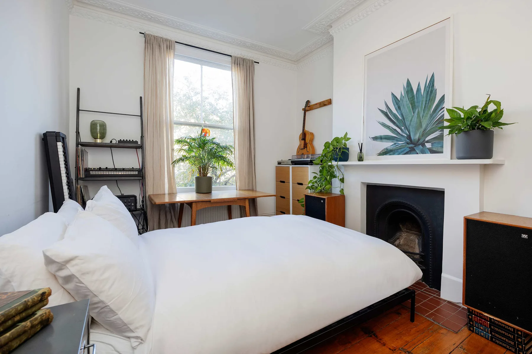 Un dormitorio luminoso con una cama blanca, una ventana y una chimenea.