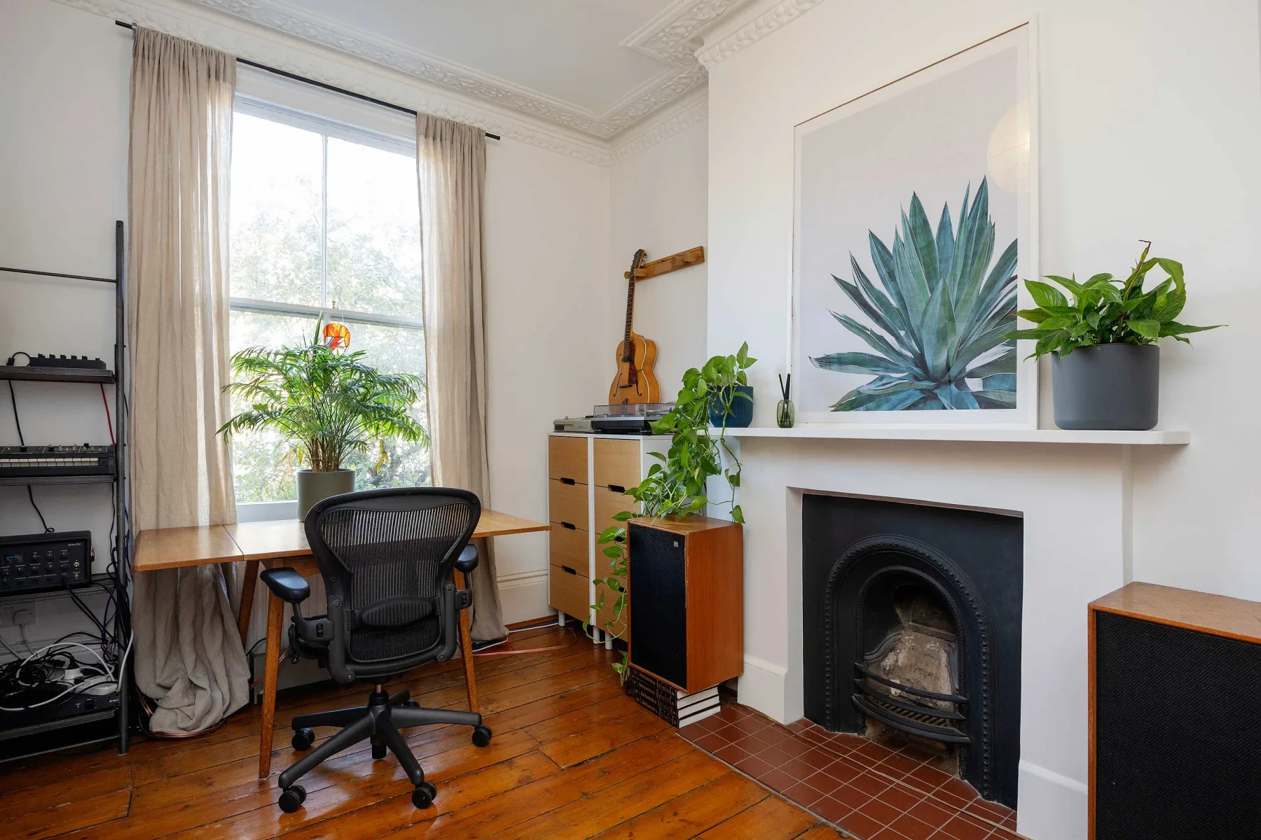 Una sala luminosa con escritorio, chimenea y plantas frondosas.
