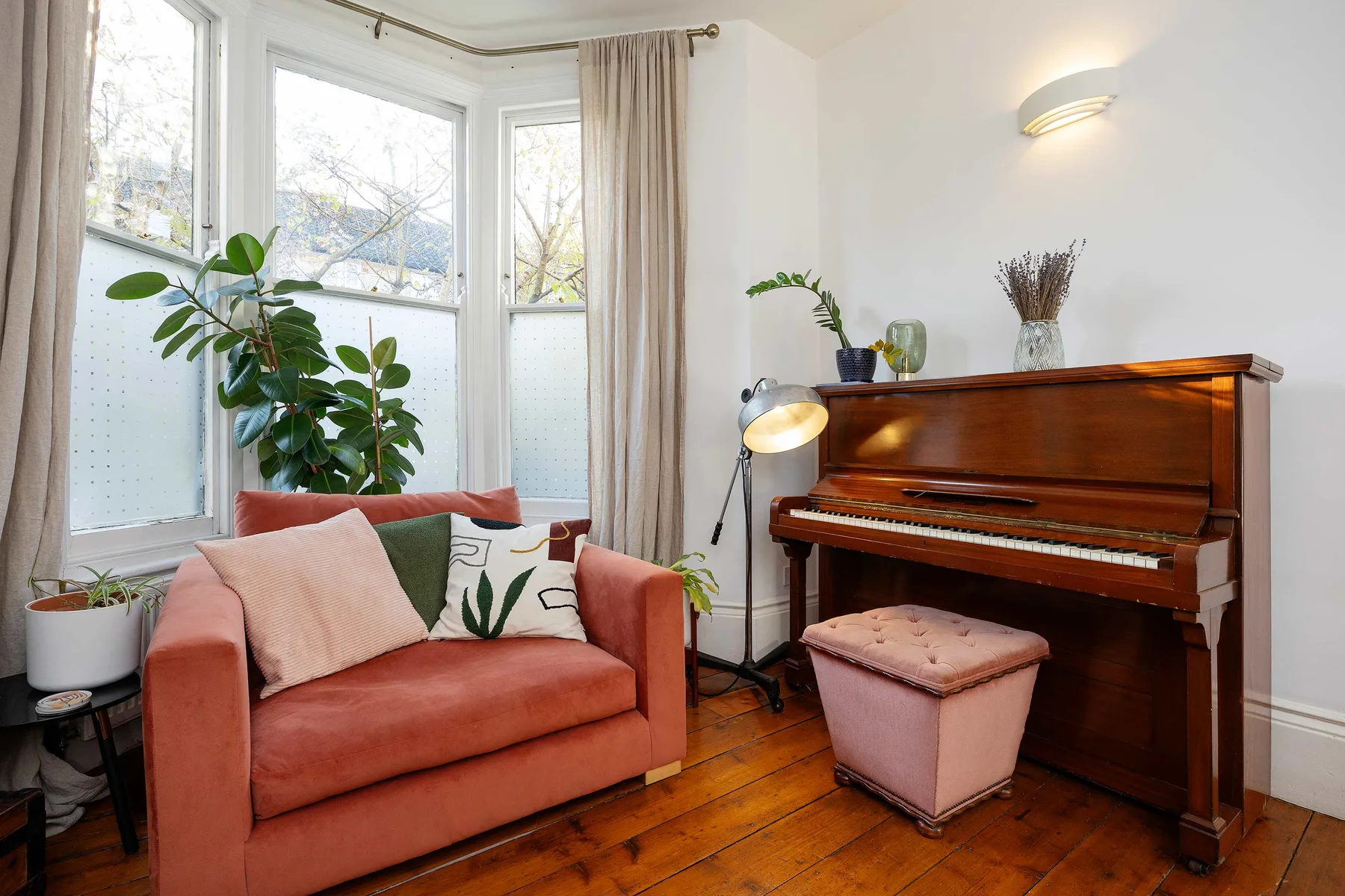 Una sala luminosa con piano, asientos color coral y ventanas grandes.