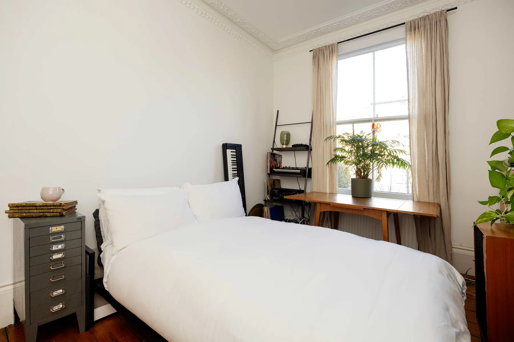 Un dormitorio luminoso con una cama bien hecha y una gran ventana con cortinas.