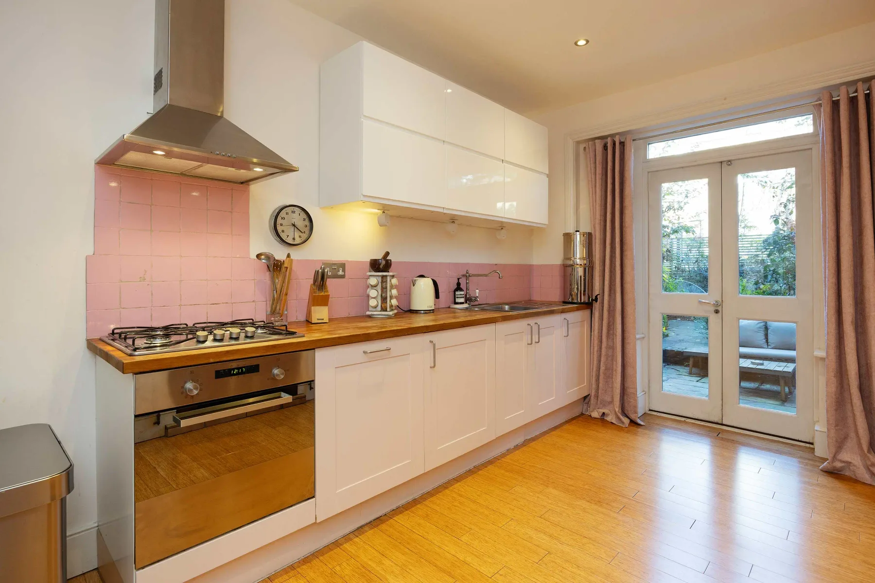 Una cocina luminosa con gabinetes blancos, encimera de madera y puertas de vidrio.