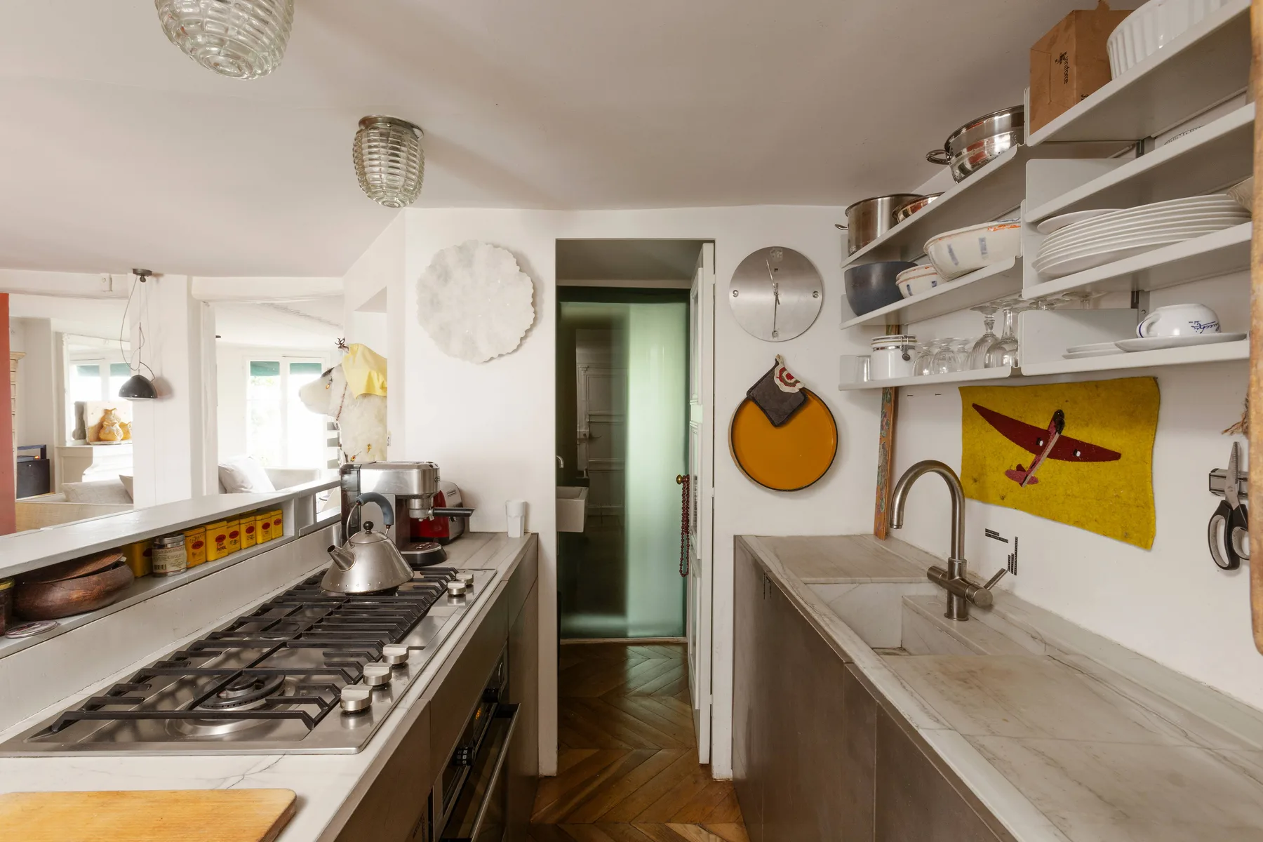 Una cocina estrecha con una larga encimera de fogones y un fregadero bajo estantes abiertos.