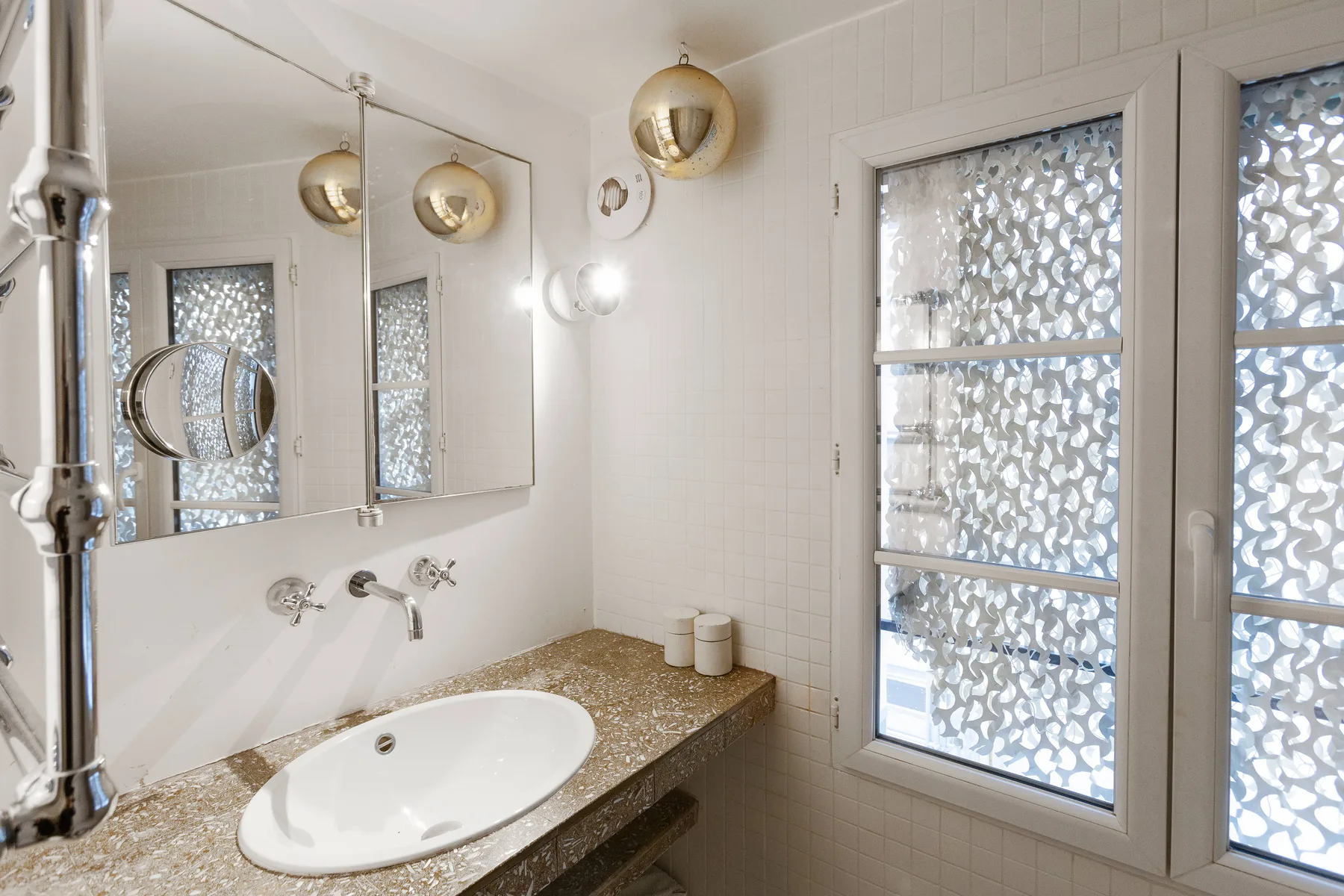 Un lavabo de baño luminoso con espejo y vidrio estampado en la ventana.