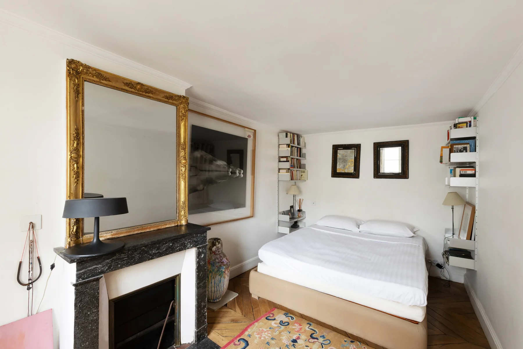 Un dormitorio con una cama, un espejo ornamentado y una chimenea.