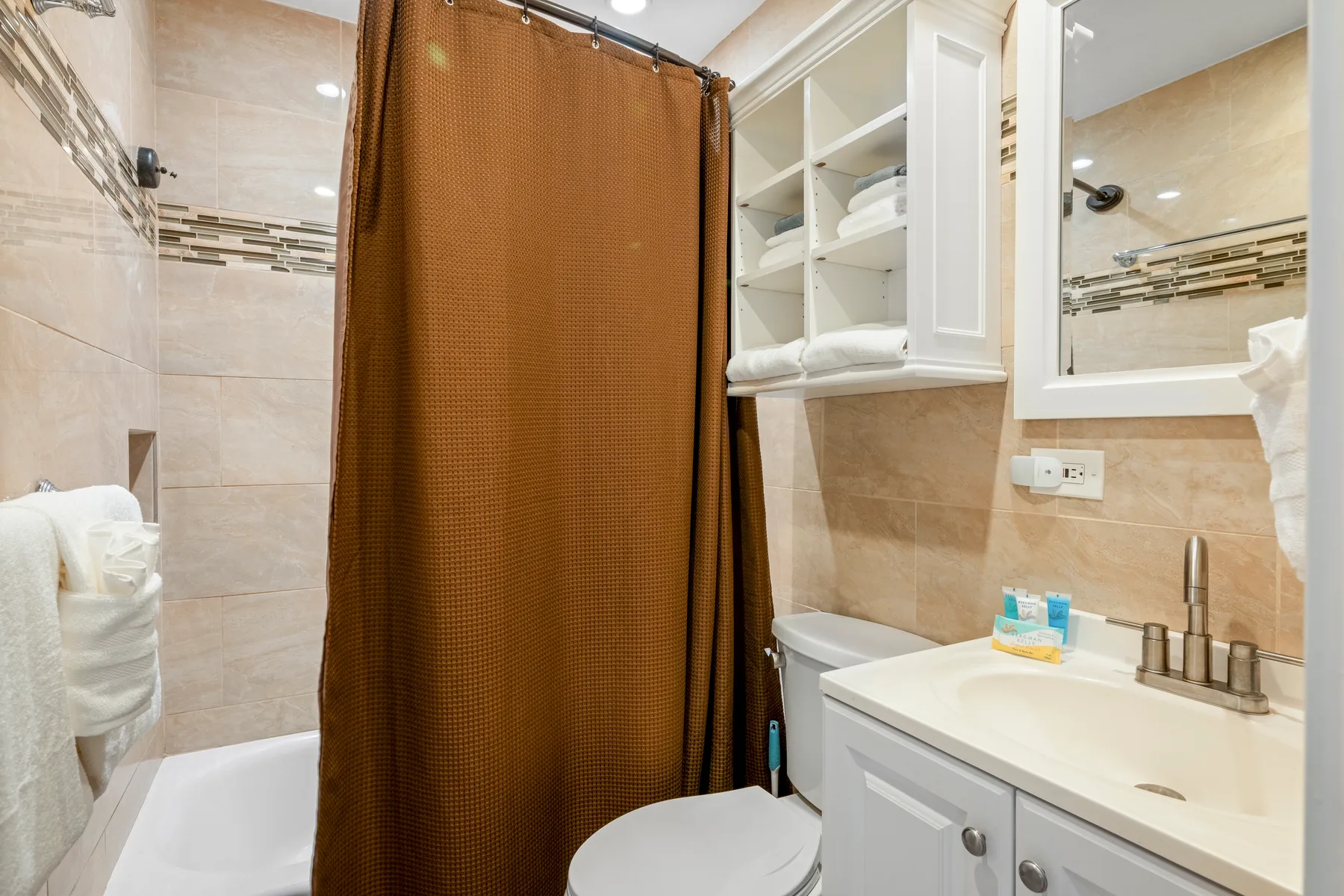 Un baño con azulejos, cortina de ducha, lavabo con mueble y estantes abiertos para toallas.