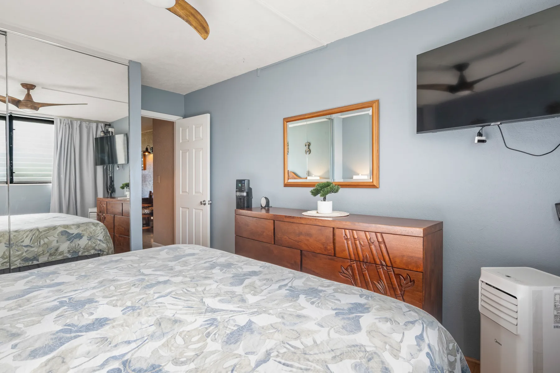 Dormitorio con cama, cómoda de madera y televisor montado en la pared.