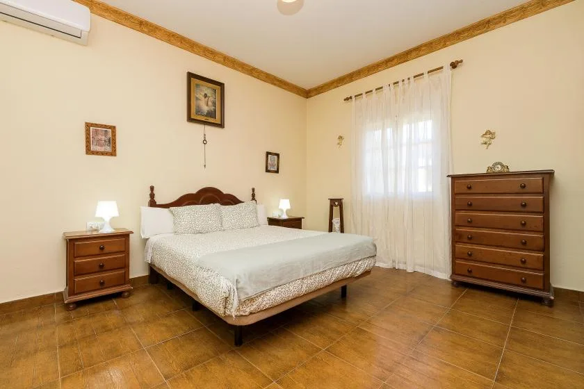 A bedroom with a double bed, wooden dressers, and a curtained window.
