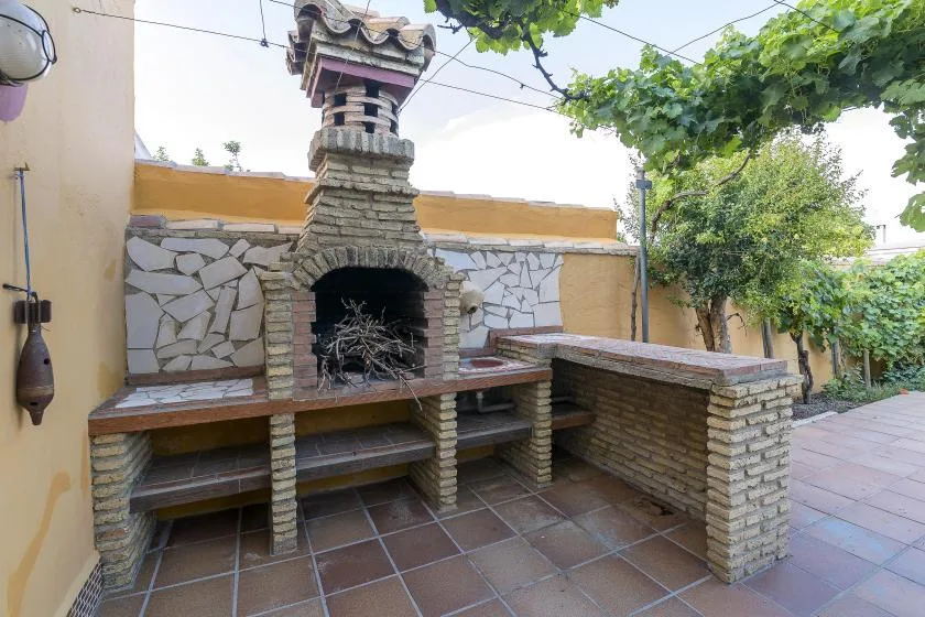 An outdoor brick barbecue area with a tiled patio and leafy vines overhead.