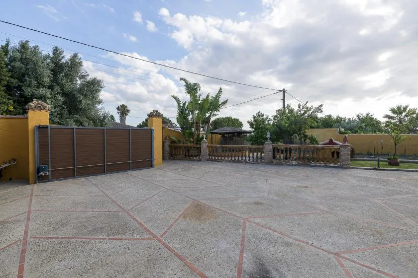 A broad paved courtyard sits beside a gated entrance and low stone railing.