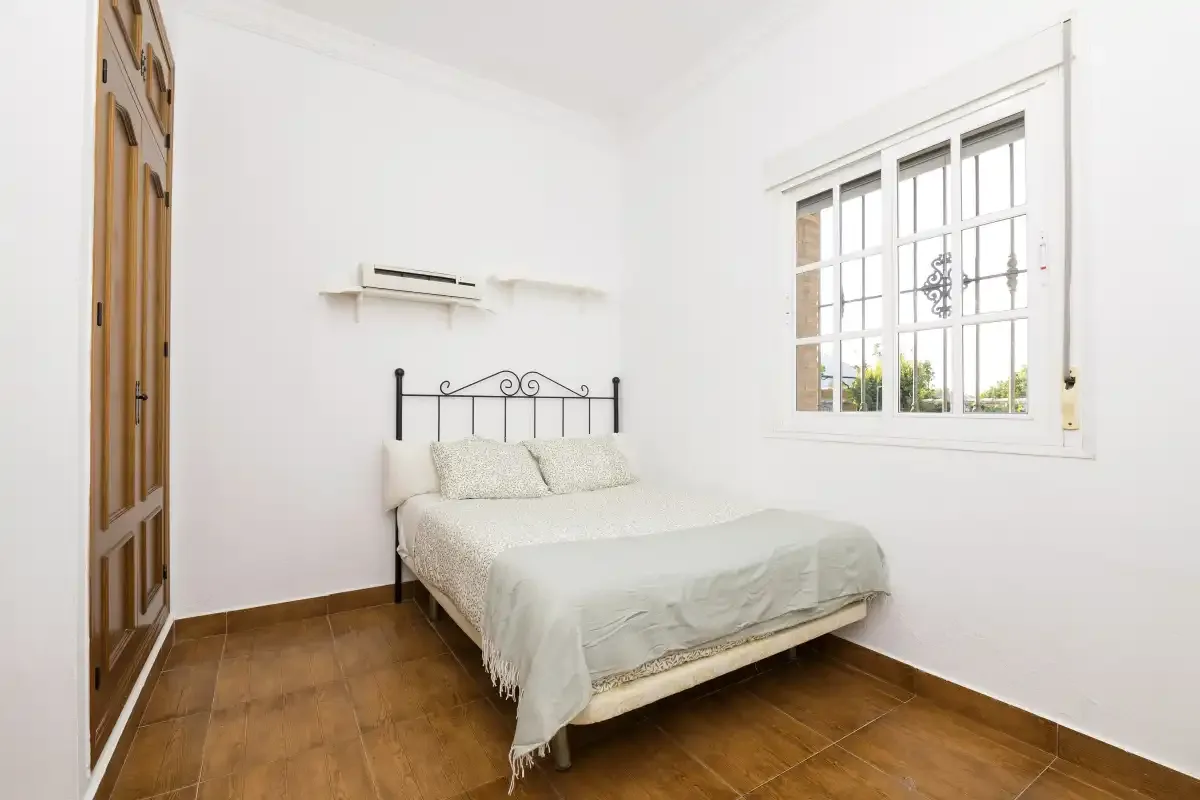 A bright bedroom with a bed beside a large window.