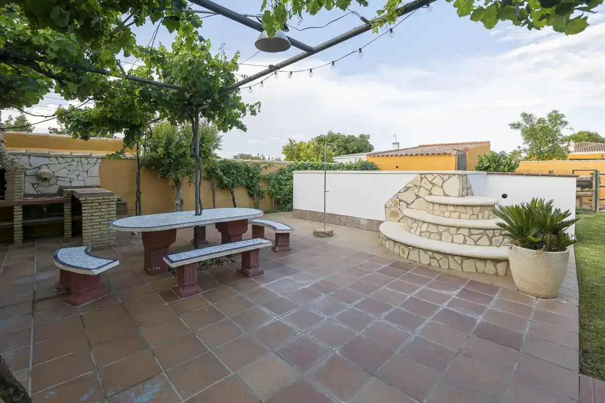 A tiled outdoor patio with a built-in stone seating area beneath leafy vines.