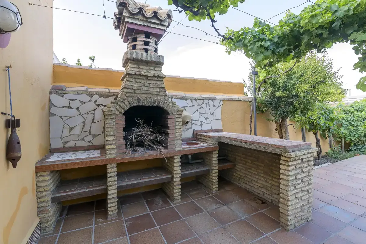 A brick outdoor barbecue area sits on a tiled patio beneath leafy vines.