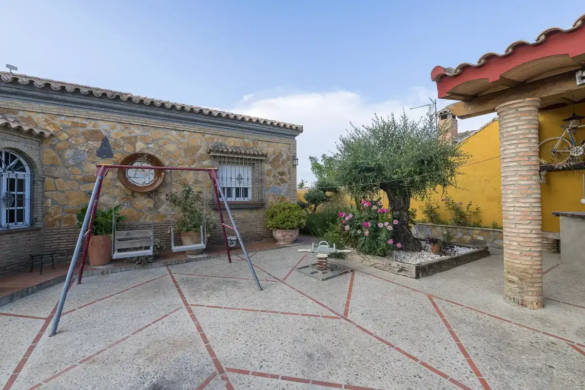 An outdoor courtyard with paved ground, garden beds, and a swing set.