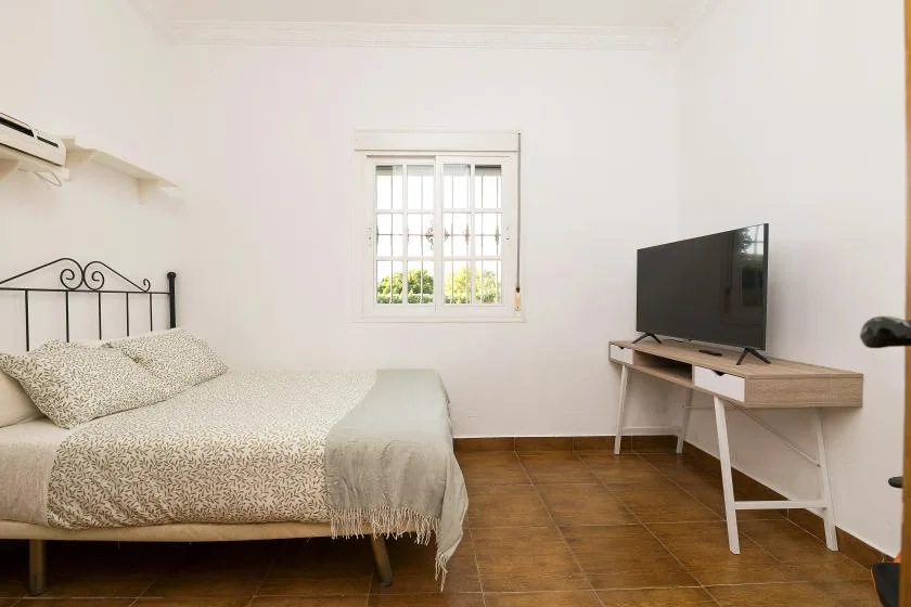 A bedroom with a bed beside a window and a television on a desk.