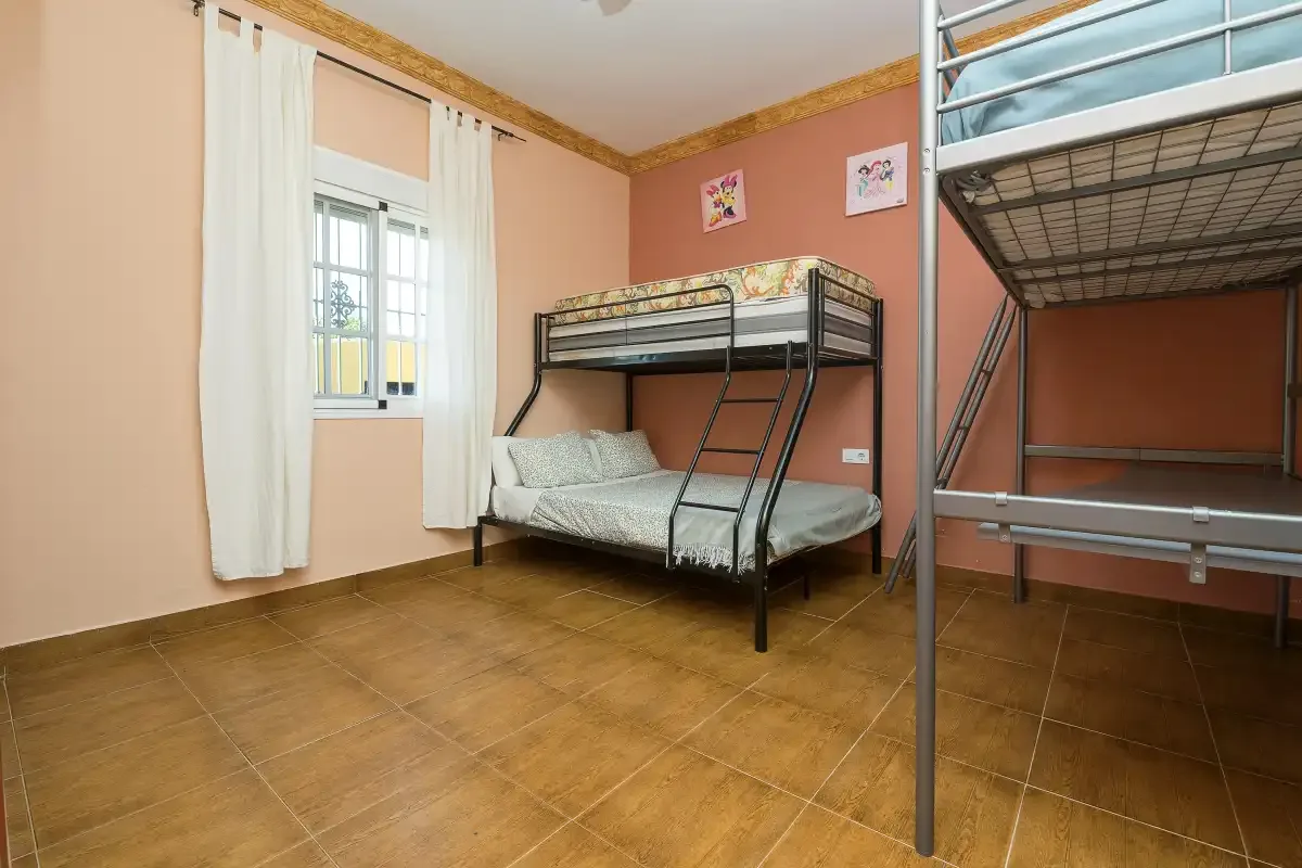A bedroom with bunk beds and a window with white curtains.