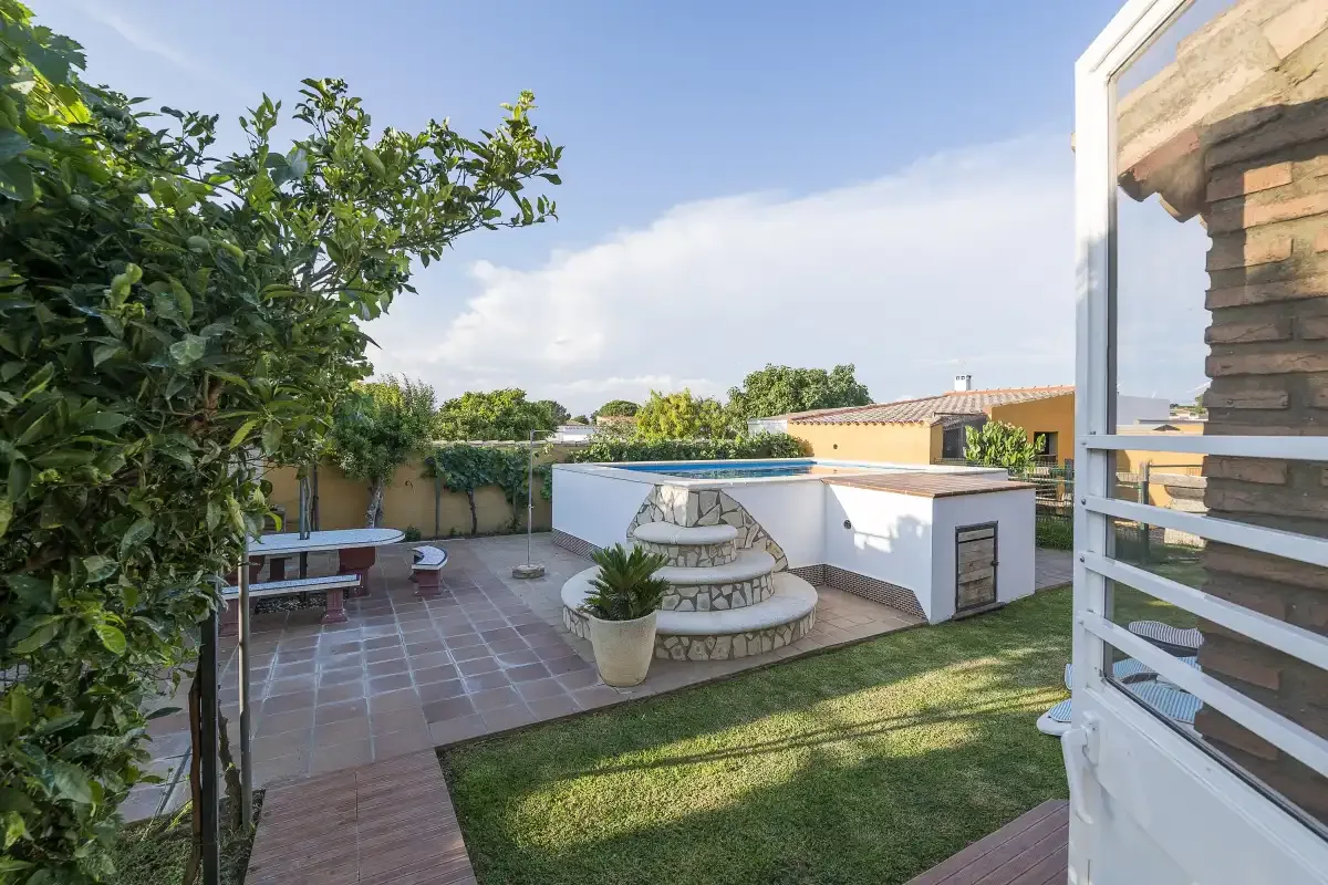 A landscaped patio with a small lawn, tiled seating area, and raised pool.