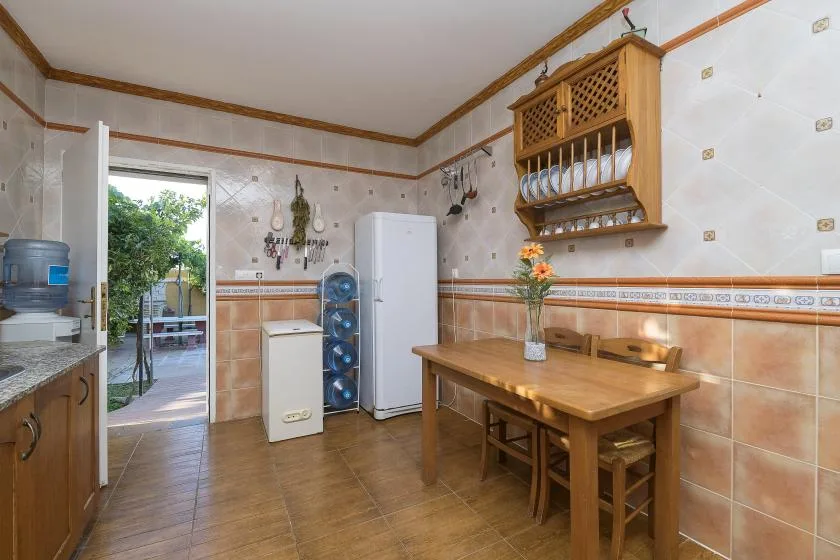 A tiled kitchen with a wooden dining table and open doorway to a garden.