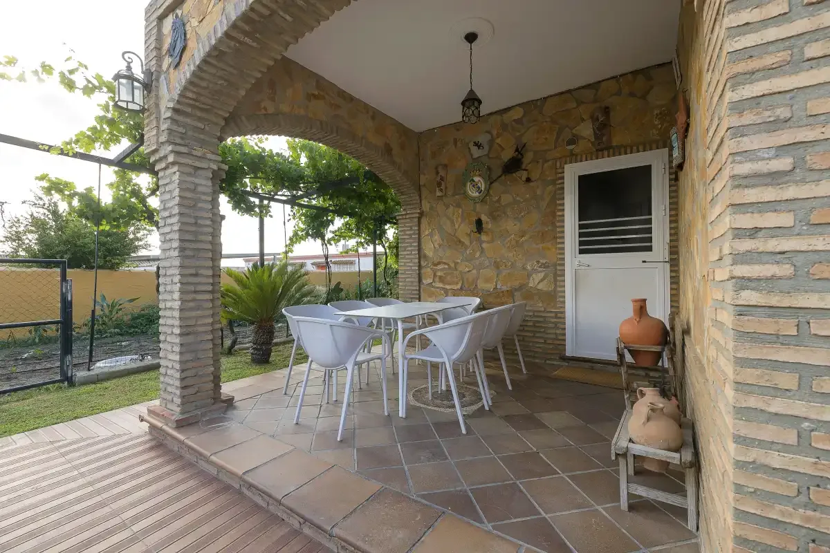 A covered patio with a dining table and chairs beside a stone wall.