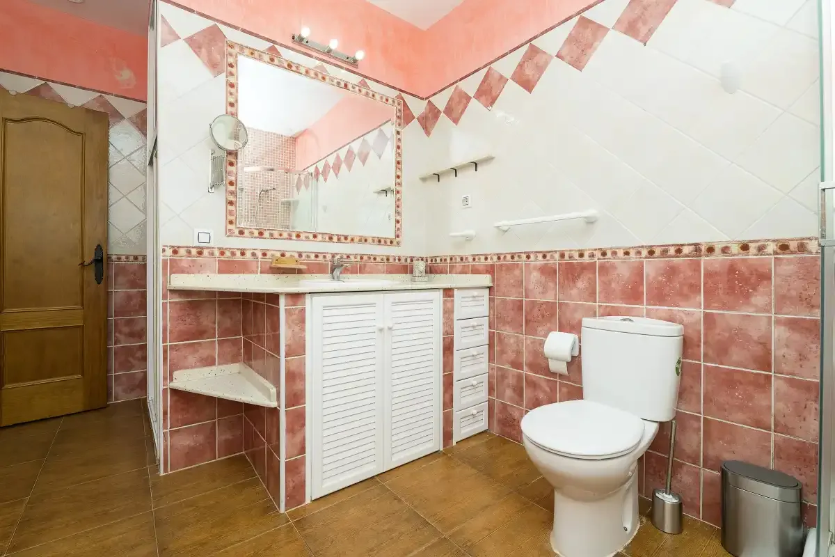 A tiled bathroom with a sink vanity, mirror, and toilet.