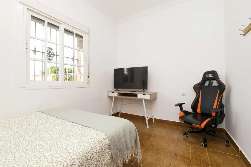A bright bedroom with a television and a black-and-orange gaming chair.